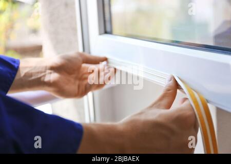 Addetto alle costruzioni che mette in casa il nastro di schiuma sigillante sulla finestra Foto Stock