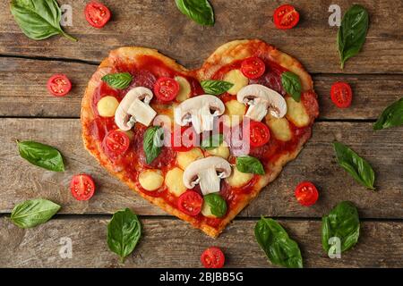 Gustosa pizza a forma di cuore con foglie di basilico e pomodori a tavola Foto Stock