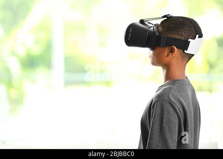 Ragazzo afro-americano che indossa occhiali di realtà virtuale su sfondo sfocato finestra Foto Stock