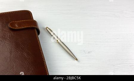 Elegante penna e pianificatore giornaliero con una copertina in pelle su una scrivania in legno bianco Foto Stock