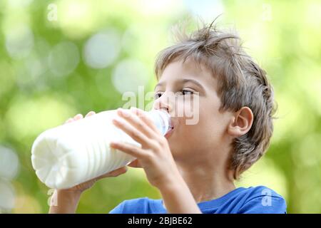 Ragazzo allegro in camicia blu bere latte da bottiglia di plastica su sfondo sfocato Foto Stock