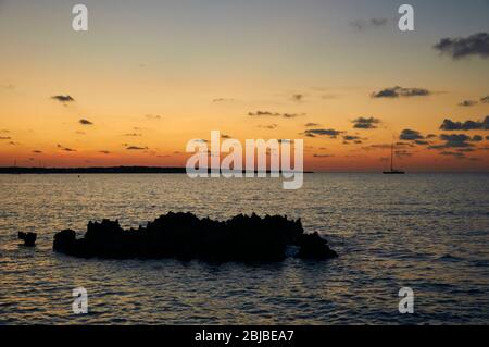 Tramonto con la silhouette rocciosa e barche a vela vicino Caló de s'Oli nel Parco Naturale di Ses Salines (Formentera, Isole Baleari, Mar Mediterraneo, Spagna) Foto Stock