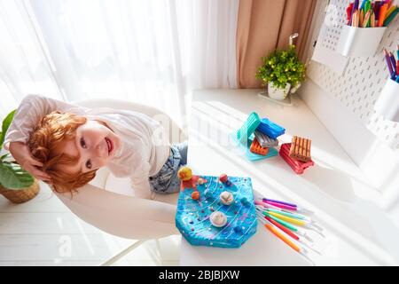felice bambino seduto alla scrivania con impianto solare artigianale, in plastilina modellante Foto Stock