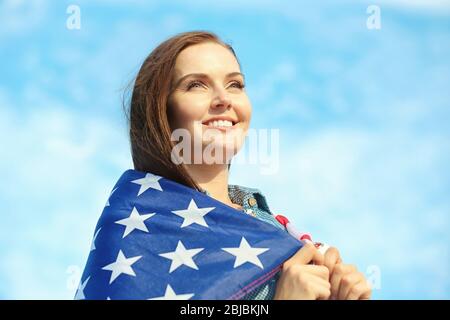 Giovane donna felice con bandiera americana su sfondo cielo Foto Stock