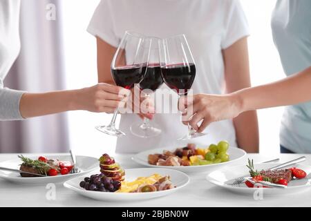 Donne bicchieri da clinking con vino e piatti deliziosi al tavolo nel ristorante Foto Stock