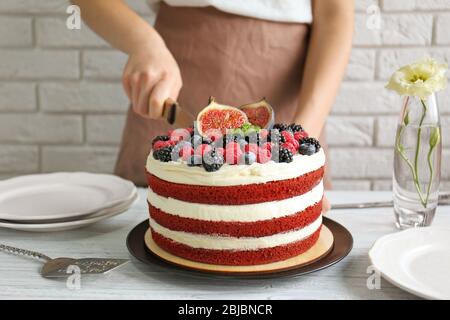 Donna che taglia gustosa torta con frutti di bosco in cucina Foto Stock