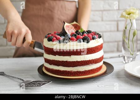 Donna che taglia gustosa torta con frutti di bosco in cucina Foto Stock