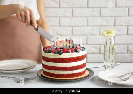 Donna che taglia gustosa torta con frutti di bosco in cucina Foto Stock