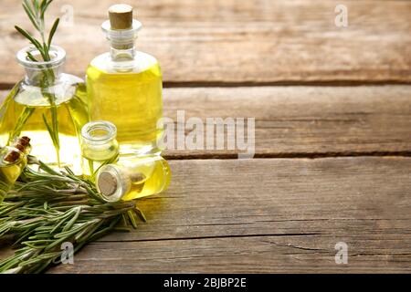 Bottiglie di olio essenziale di conifere e rami di rosmarino su sfondo in legno, vista ravvicinata Foto Stock