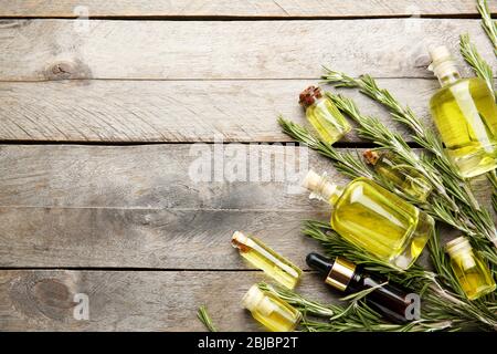 Bottiglie di olio essenziale di conifere e rami di rosmarino su fondo ligneo Foto Stock