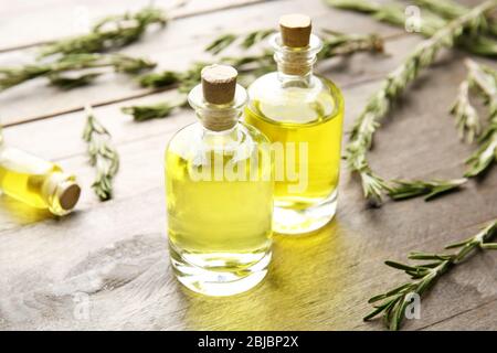 Bottiglie di olio essenziale di conifere e rami di rosmarino su sfondo in legno, vista ravvicinata Foto Stock
