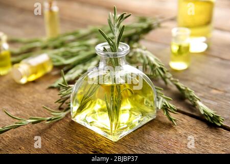 Bottiglia di olio essenziale di conifere e rami di rosmarino su sfondo in legno, vista ravvicinata Foto Stock