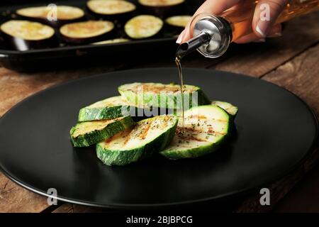 Mano femminile che versa olio su fette di zucca Foto Stock