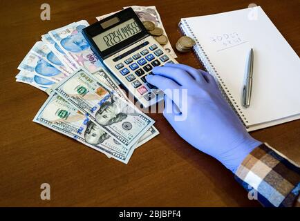 Mano in guanti debiti sulla calcolatrice contro sfondo di denaro Foto Stock