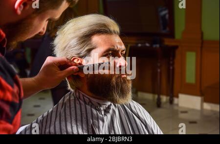 Uomo al barbiere. Parrucchiere. Barbiere e cliente professionale. Rifinitura della barba da vicino. Mantenimento della forma della barba. Migliora la tua esperienza di taglio dei capelli. Capelli facciali. Crescere barba e baffi. Foto Stock