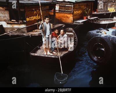 Hong Kong Ottobre 1986 i bambini in barca nel porto di Aberdeen catturano denaro passando le barche. La foto fa parte di una collezione di fotografie scattate a Hong Kong tra settembre e novembre 1986. Rappresentano un'istantanea della vita quotidiana nella colonia della corona undici anni prima che la sovranità fosse trasferita di nuovo alla Cina continentale. Fotografia di Howard Walker / Alamy. Foto Stock