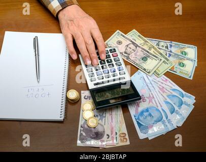 mano di calcolo, denaro di carta e monete su una tavola di legno. Foto Stock