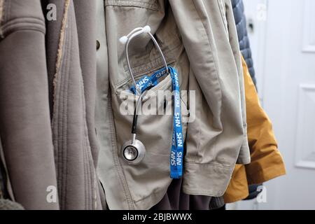 stetoscopio del medico e cordino nhs nella tasca del cappotto appeso nel corridoio della casa Foto Stock