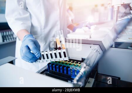 Il personale medico in laboratorio colloca il campione di sangue per l'esame nell'analizzatore automatico. Concept DNA test, rilevazione virus. Sfondo blu chiaro Foto Stock