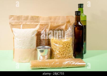 Stock di prodotti alimentari in imballaggi di carta e cellophane su beige-verde. Cereali, pasta, bottiglie d'olio. Concetto di stoccaggio degli alimenti zero-waste. Senza plastica. St Foto Stock