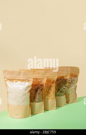 Fila di sacchetti di carta con cellophane pieno di cereali e legumi sullo sfondo beige. Concetto di stoccaggio degli alimenti zero-waste. Senza plastica. Scorta per un giorno piovoso. S Foto Stock