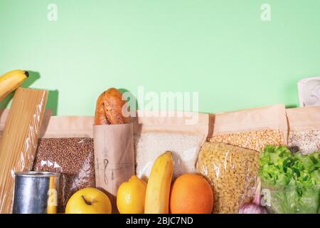 Stock di prodotti alimentari in imballaggi ecologici e frutta disposti su sfondo verde. Cereali, pasta, lattina, pane, banane, mele, arancia, limone, insalata. Foto Stock
