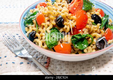 Fusilli lunghi, pomodoro di ciliegia, olive nere e spinaci, cibo mediterraneo per la dieta. Foto Stock