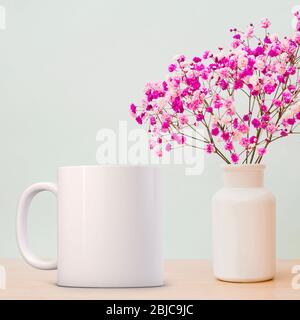 Mug Mockup bianco, accanto ad un singolo fiore in un vaso di vetro. Perfetto per le aziende che vendono tazze, basta sovrapporre la vostra citazione o il design sopra l'immagine. Foto Stock