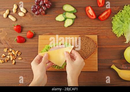 Mani femminili che fanno un gustoso sandwich su tavola di legno Foto Stock