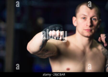 Sport: Il kickboxer dell'uomo sta esercitandosi nel calcio in una palestra di boxe Foto Stock