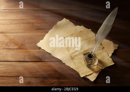 Penna in piuma con inkwell e documenti in bianco su sfondo di legno Foto Stock