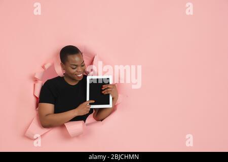 Mostra lo schermo vuoto del tablet, sorridente. Giovane afro-americana posa in sfondo carta corallo lacerato, emotivo. Rompersi, infranti. Concetto di emozioni umane, espressione facciale, vendite, annuncio. Foto Stock