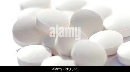 Mucchio di pillole bianche semplici e rotonde, gruppo di piccole compresse su bianco, macro, primo piano, concentrarsi su una pillola. Nuovi farmaci, integratori e farmaci Foto Stock