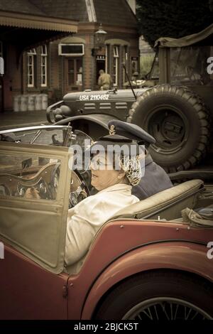 Primo piano coppia anni '40 in auto vintage open-top in arrivo alla stazione ferroviaria Severn Valley Heritage, Kidderminster anni '40 in tempo di guerra evento estivo, Regno Unito. Foto Stock