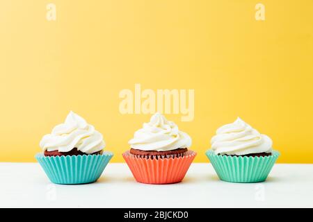 Tre cupcake di velluto rosso colorati su sfondo giallo Foto Stock