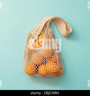 Sacchetto a rete con frutta su sfondo blu. Shopping moderno e riutilizzabile e concetto di zero sprechi. Ritaglio quadrato Foto Stock