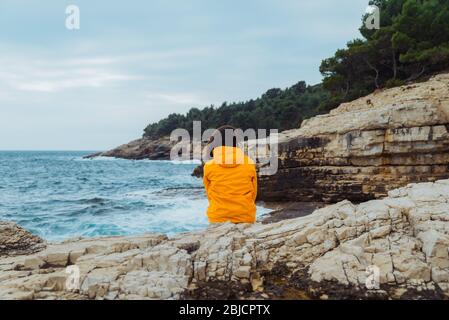 La donna posa sul bordo della scogliera alla ricerca sulle grandi onde Foto Stock