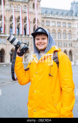 uomo in impermeabile giallo con grande fotocamera dslr a piazza della città Foto Stock