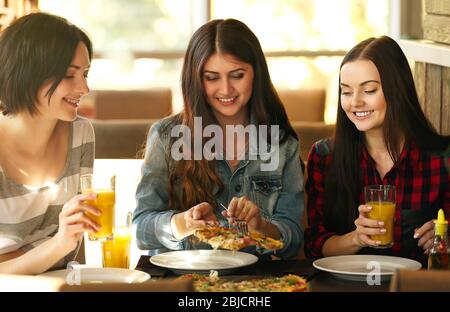 Giovani donne allegre seduti in un bar con pizza e succo di frutta Foto Stock