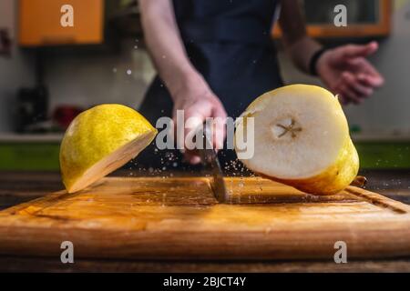 Chef che taglia a metà una pera gialla matura con un grosso coltello in movimento. Spruzzi di acqua e succo volare in diverse direzioni e congelare in aria Foto Stock
