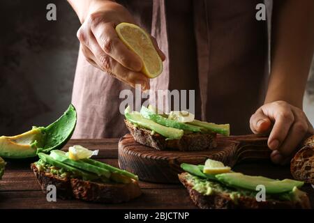 Donna che fa deliziosa bruschetta con avocado e limone su tavola di legno Foto Stock