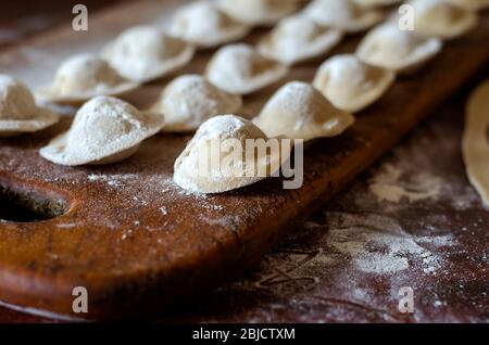 Gnocchi crudi con carne su un tagliere di legno con farina. Ravioli fatti in casa primo piano. Cibo fatto in casa. Messa a fuoco selettiva. Foto Stock