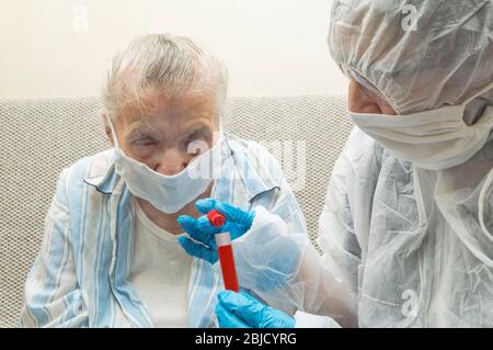 L'operatore sanitario produce sangue da una donna anziana potenzialmente infetta per il controllo del test a covid 19. Medicina e concetto di salute. Foto Stock