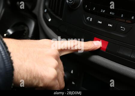 Maschio a mano di emergenza premendo il pulsante di avvertimento sulla console di auto, primo piano Foto Stock