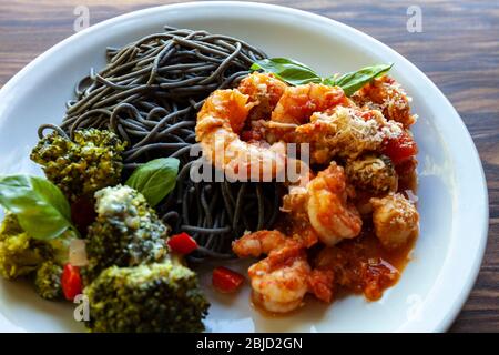 Spaghetti neri con salsa di pomodoro ai gamberi e broccoli al forno con formaggio Roquefort Foto Stock