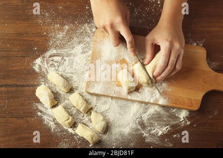 Donna che taglia l'impasto crudo sul tavolo da cucina, primo piano Foto Stock