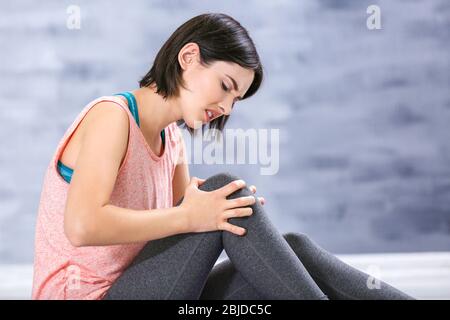 Bella giovane donna che soffre di dolore al ginocchio in casa Foto Stock