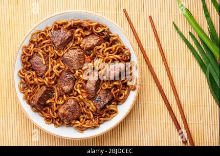 Pasta RAM-Don o Chapaguri con bistecca di manzo in ciotola bianca. Jjapaguri è un popolare piatto sudcoreano con spaghetti ramen e udon e bistecca di manzo. Copia Foto Stock