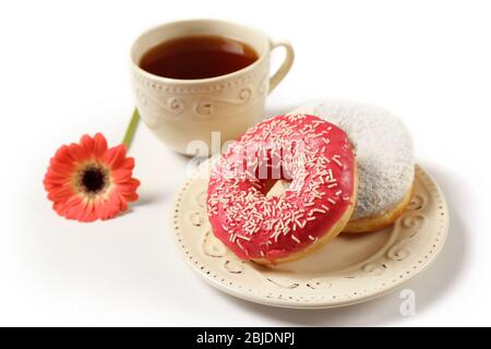 Piatto con deliziose ciambelle, tazza di caffè e fiore su sfondo bianco Foto Stock