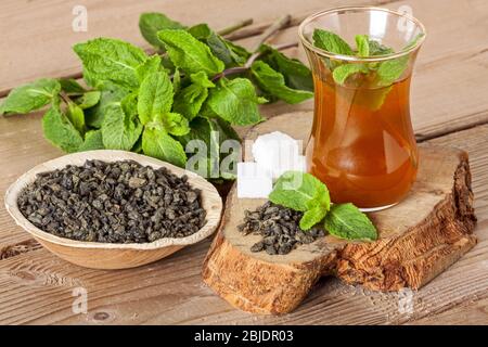 Tè marocchino con menta e zucchero in un bicchiere su sfondo di legno. Foto Stock